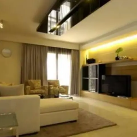 Living room with a white L-shaped sofa and glass coffee table facing a wood-panelled TV console lit by a warm cove-lit backdrop.