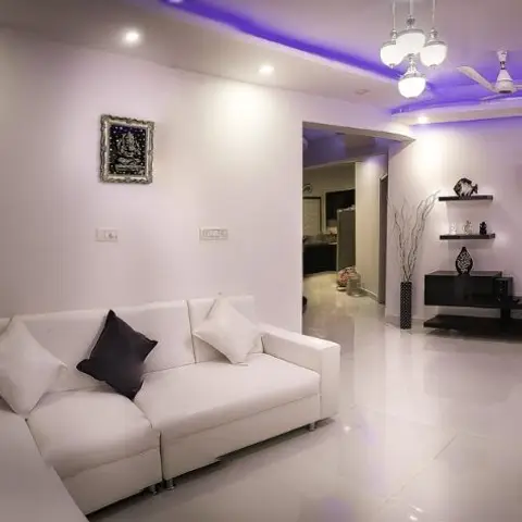 Living room with a white leather sectional sofa, a geometric cube shelving TV unit, and a cove ceiling lit in blue-purple LED accent lighting.