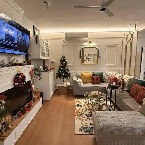 Living room with a white panel-moulded wall, mantel-style TV console, sectional sofa and a floral area rug on wood-look flooring, decorated for the holidays.