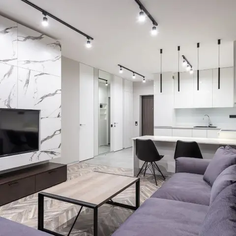 Living room with a white-veined marble slab TV feature wall, herringbone wood flooring and a purple sectional sofa, kitchen visible beyond