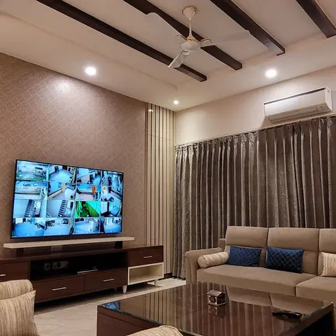 Living room with a wood-beam false ceiling, textured wallpaper feature wall behind a wall-mounted TV over a walnut console, and heavy curtains.