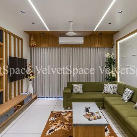Living room with a wood-clad cove-lit ceiling, a slatted wood partition housing an open-shelf TV unit, and an olive-green sectional sofa on a floral rug.