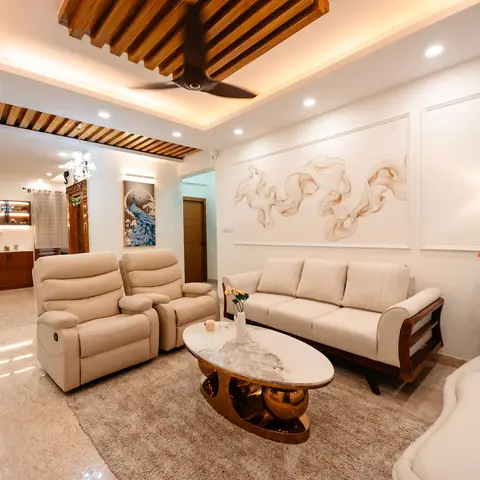 Living room with a wood-slat coved false ceiling, cream reclining sofa set, and an oval marble-and-gold coffee table on a beige shag rug.
