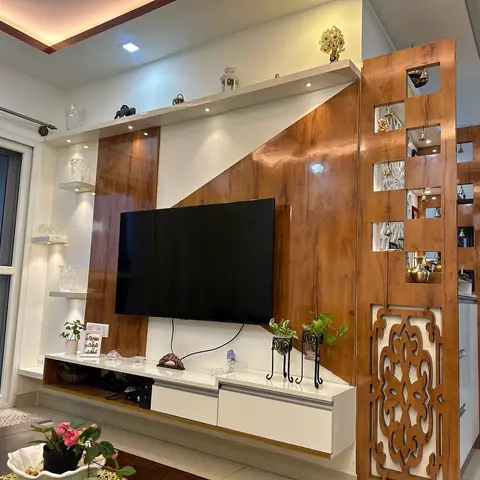 Living room with a wood-veneer and white lacquer TV unit beside a carved wooden jaali partition strung with hanging brass bells