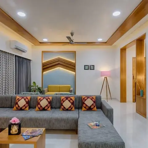 Living room with a wraparound grey L-sofa and diamond-motif cushions, a backlit chevron wood niche framing a yellow bench seat