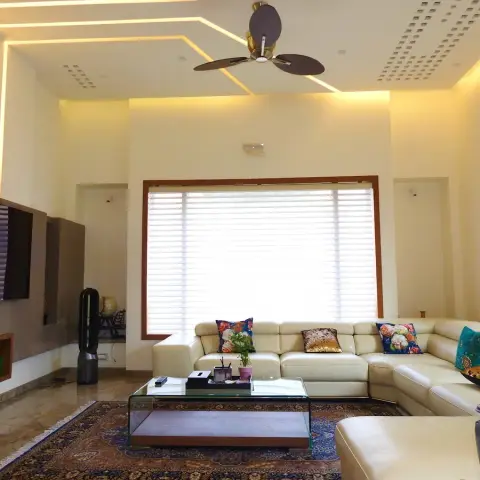 Living room with an angular cove-lit false ceiling, a cream leather sectional sofa with colourful cushions