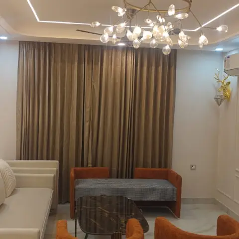 Living room with an arched cove-lit wall niche, a branching glass-globe chandelier, and rust-orange armchairs flanked by gilt stag-head wall mounts.