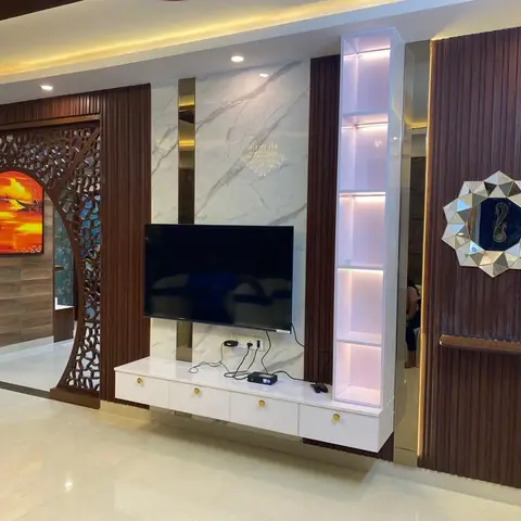 Living room with an elaborate carved wood jaali archway leading to another room, a marble-and-fluted-panel TV feature wall with a backlit display niche