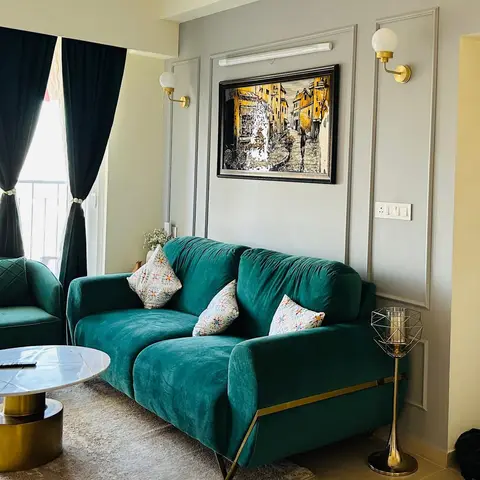Living room with an emerald velvet sofa and armchair trimmed in brass, a round white marble coffee table on a brass base, wall panel moulding