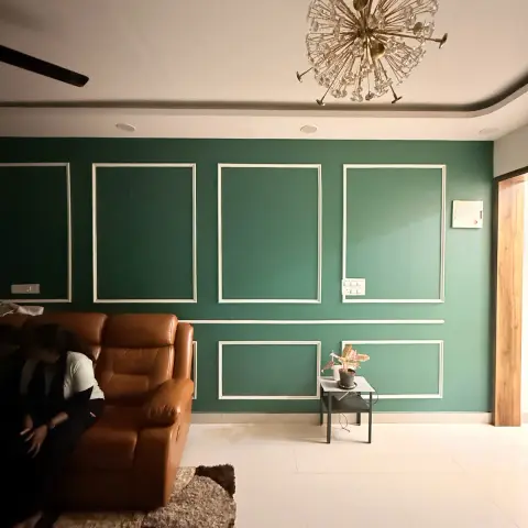 Living room with an emerald wall laid out in slim white moulding frames above a chair rail, a tan leather recliner sofa on a shaggy rug