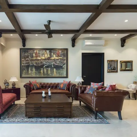 Living room with an exposed dark wood beam-and-corbel ceiling, tufted brown leather chesterfield sofas, a pink floral chaise