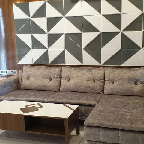 Living room with an L-shaped grey button-tufted sofa facing a geometric black-and-white triangular tile feature wall.
