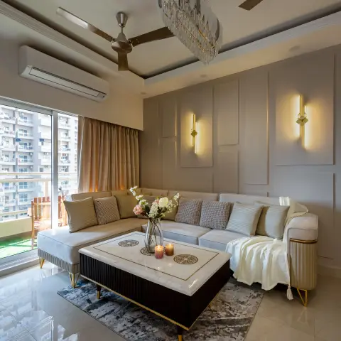 Living room with an L-shaped sectional sofa around a black-and-marble coffee table, a feather-and-crystal chandelier, and gold wall sconces on panelled walls.