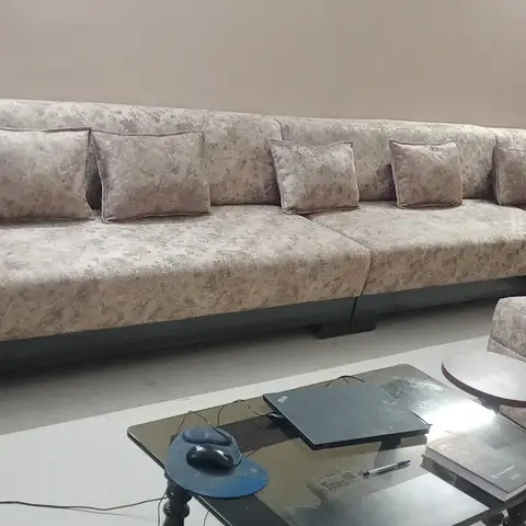 Living room with an L-shaped floral-upholstered sectional sofa and matching ottoman around a glass coffee table cluttered with a laptop and papers