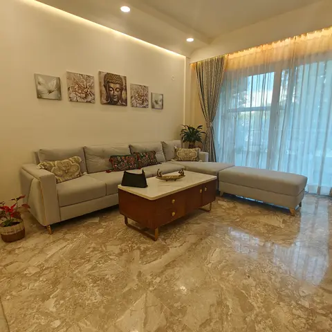 Living room with an L-shaped grey sofa beneath a five-piece gallery wall centered on a Buddha print, glossy beige marble flooring.