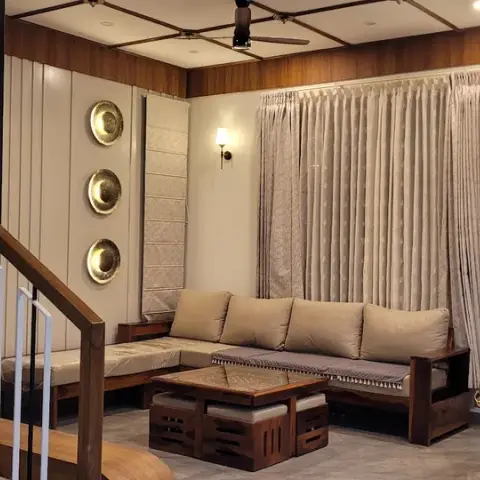Living room with an L-shaped wood-frame sofa, a brass-chained hanging swing, three brass wall plates, and a wood-panelled coffered ceiling.