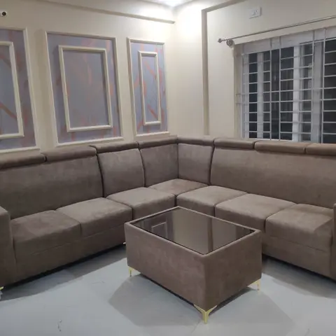 Living room with an L-shaped taupe sectional sofa, a glass-top upholstered coffee table on brass legs, and three framed geometric wall panels above the seating.