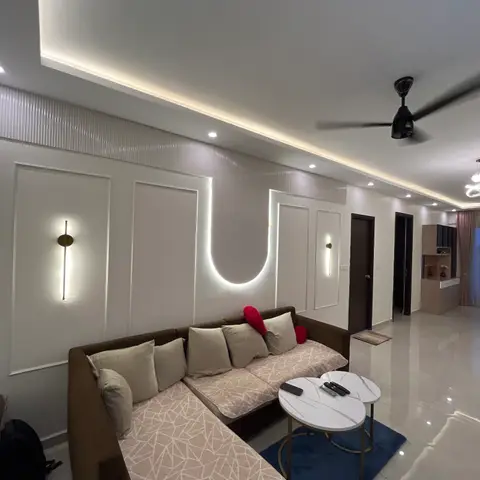 Living room with an L-shaped beige sectional sofa, a wall panel with a glowing U-shaped LED cutout, cove-lit ceiling, brass wall sconces