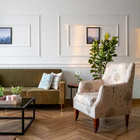 Living room with an olive channel-tufted velvet sofa and a tree-print floral wingback armchair on a herringbone wood floor