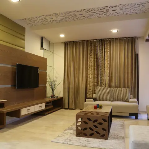 Living room with an olive-green channel-tufted leather accent wall, a laser-cut jaali ceiling border, and gold damask curtains behind cream sofas.