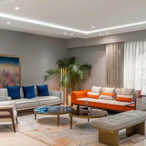 Living room with an orange velvet sofa and a cream wingback armchair around twin marble-top coffee tables, navy accent pillows