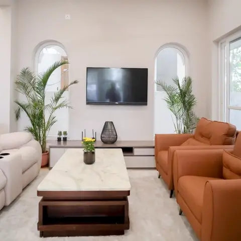 Living room with arched window surrounds, a cream reclining sofa opposite terracotta leather armchairs, and a white marble-top coffee table on a dark wood base.
