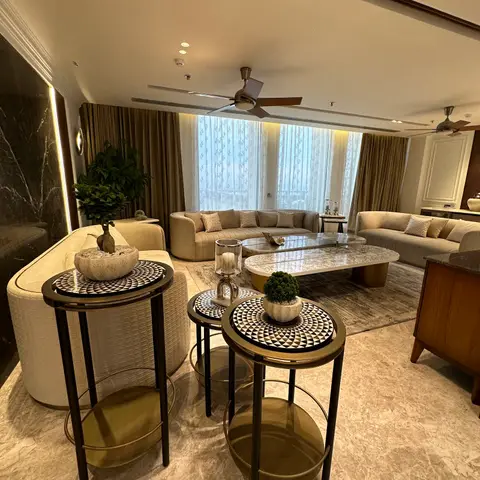 Living room with beige sofas around an oval marble coffee table, a dark veined marble accent wall, sheer curtains at floor-to-ceiling windows