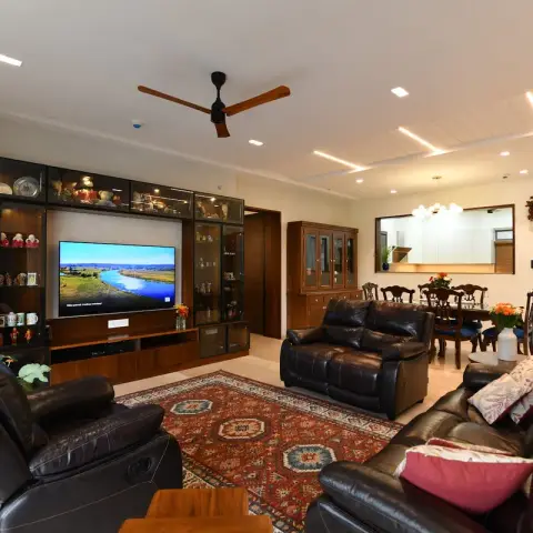 Living room with black leather reclining sofas and a Persian-style rug, a dark-wood TV unit flanked by glass-front display cabinets