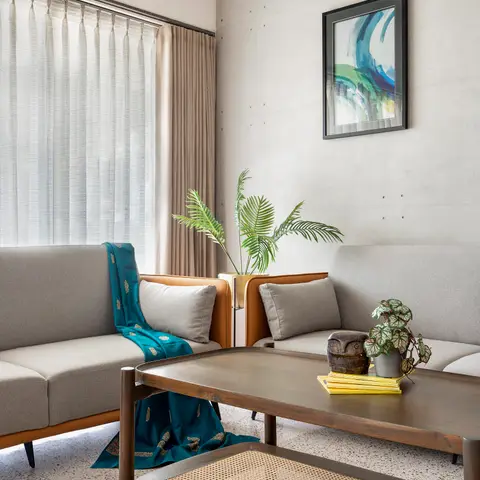 Living room with board-formed concrete walls, a terrazzo floor, and mid-century-style grey sofas around a wood-and-cane coffee table.