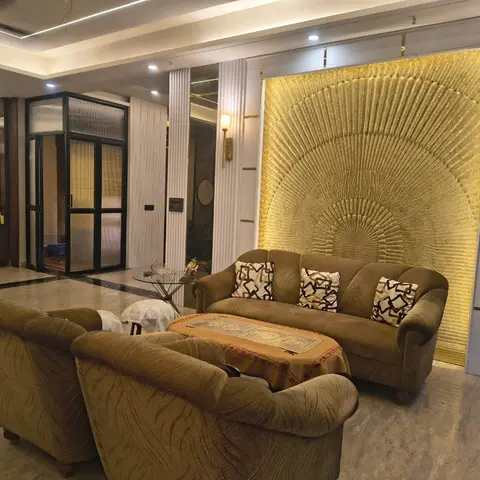 Living room with brown patterned sofas facing a dramatic gold radial-textured backlit feature wall, a glass coffee table, and marble flooring