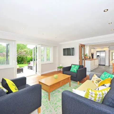 Living room with charcoal-grey sofas and yellow-green accent cushions, plantation shutters, and a garden view through folding doors