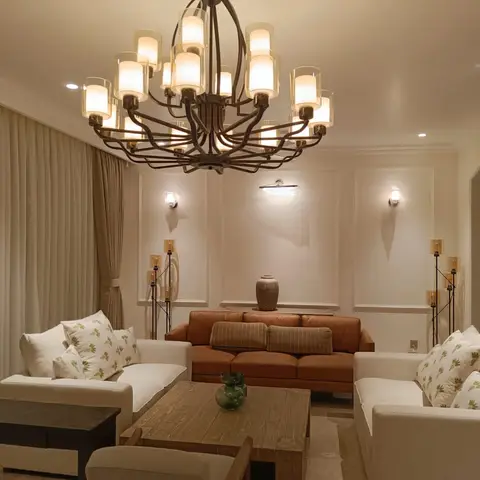 Living room with cognac leather and cream sofas around a reclaimed-wood coffee table, beneath a large candelabra-style chandelier and panel-moulded walls.