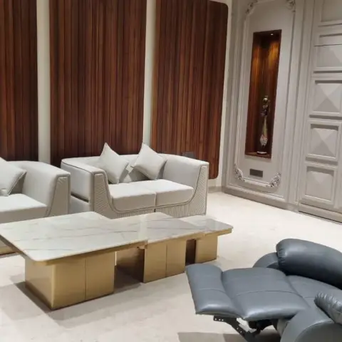 Living room with cream leather sofas trimmed in gold, a marble-and-brass coffee table, and a fluted walnut panelling wall beside a 3D geometric feature wall.