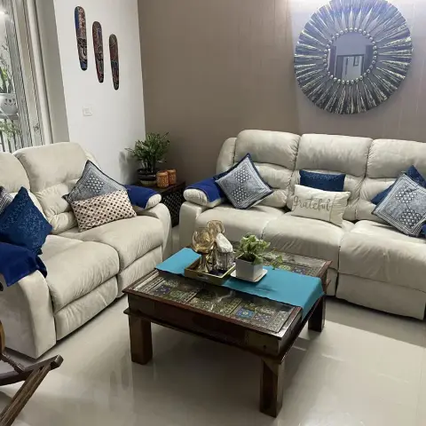 Living room with cream reclining sofas dressed in indigo cushions, a brass-inlaid wood coffee table, and a sunburst mirror above a taupe accent wall.