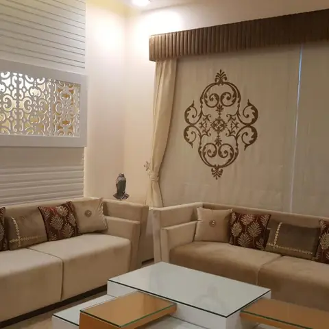 Living room with cream velvet sofas dressed in maroon and gold embroidered cushions, a backlit CNC-cut jaali wall panel, damask-motif curtain panels