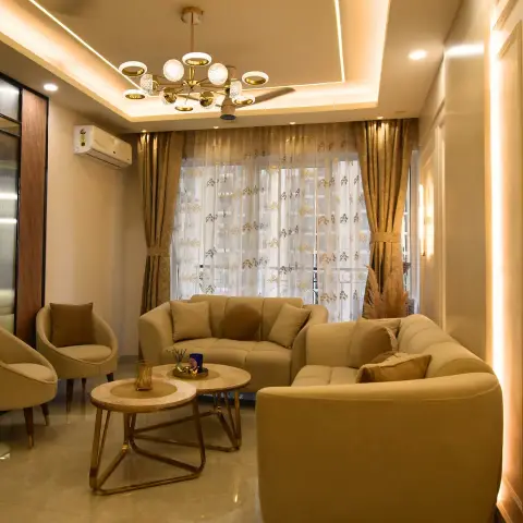 Living room with curved beige sofas, round gold-and-marble coffee tables and a brass sputnik chandelier beneath a cove ceiling.