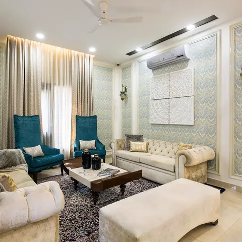 Living room with damask wallpaper panels framed in moulding, a tufted chesterfield-style sofa and teal velvet wingback chairs