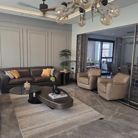 Living room with dark brown leather sofas and tan armchairs around two-tone coffee tables, panel-moulded feature wall