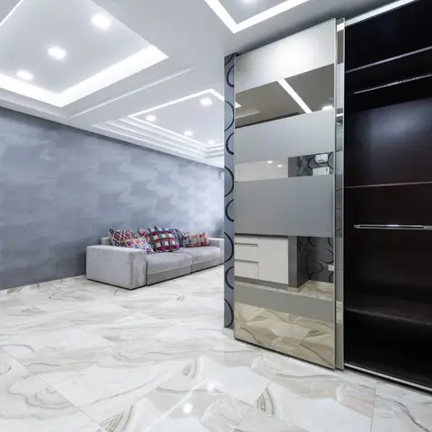 Living room with dramatic swirl-textured dark wall panelling, a geometric cove-lit POP ceiling, a grey sofa with multicolour cushions