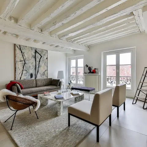 Living room with exposed whitewashed ceiling beams, a large abstract canvas, a marble coffee table, and a mix of vintage sling and upholstered chairs.