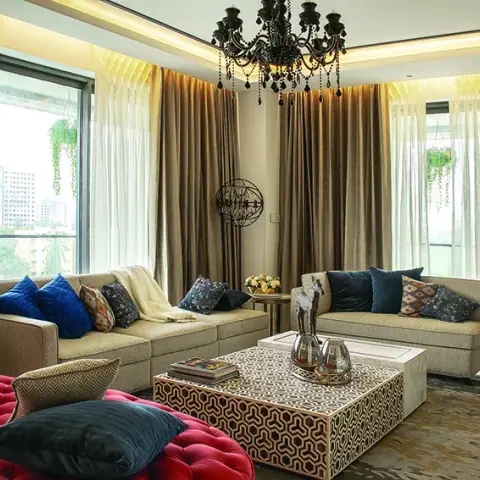 Living room with facing beige sectional sofas in blue and patterned cushions around a geometric-inlay coffee table, under a black beaded chandelier