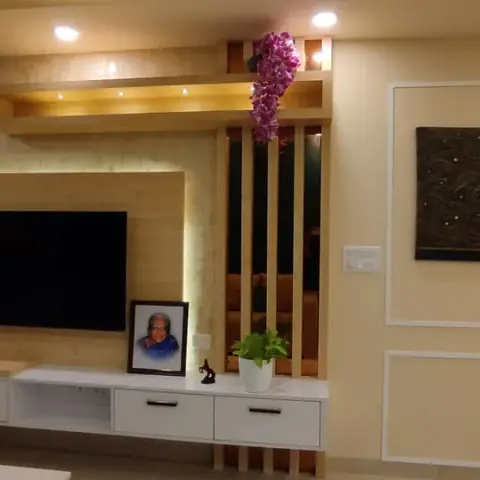 Living room with family photographs propped along a white drawer console under a backlit beige wood TV panel