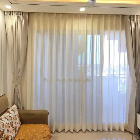 Living room with floor-to-ceiling sheer-and-heavy drapery framing a large window, a brown sofa styled with floral cushions