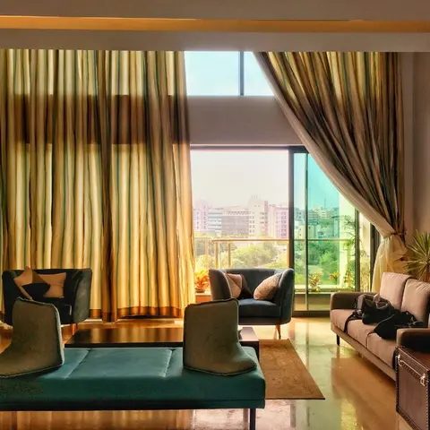Living room with floor-to-ceiling striped curtains, teal velvet armchairs and a matching bench, a red abstract painting on the side wall and a city view