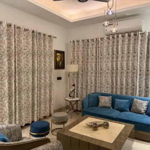 Living room with floor-to-ceiling floral-patterned curtains, a teal velvet sofa and armchair with textured cushions