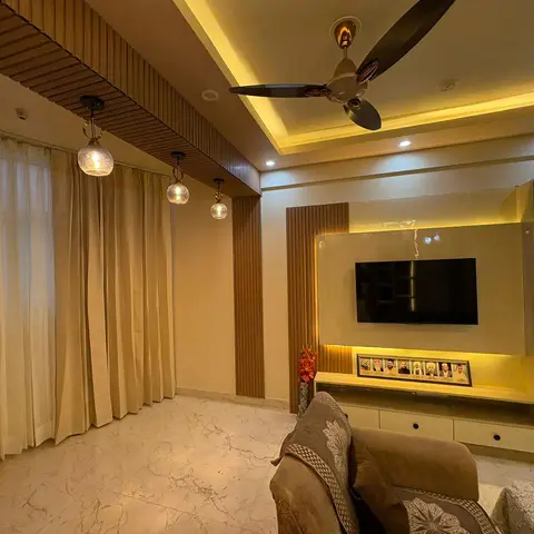 Living room with fluted wood panelling behind a cove-lit TV wall and a lit glass display cabinet, marble flooring and sheer curtains along the window wall.