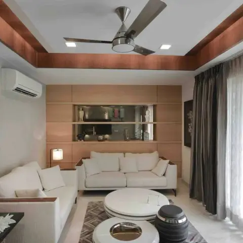 Living room with fluted wood wall panelling and a warm wood cove-lit ceiling, cream sofas around round nesting coffee tables and a built-in display shelf