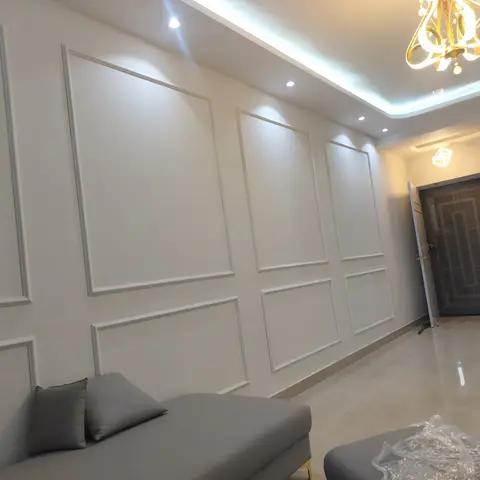 Living room with framed wall-panel moulding along the entry wall, a cove-lit ceiling and a crystal-drop chandelier near the main door.