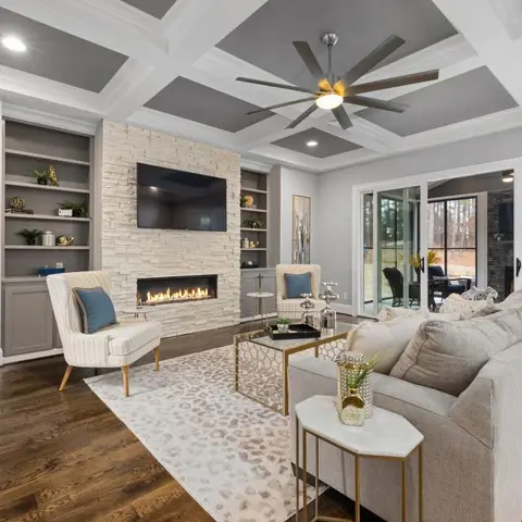 Living room with grey-and-white coffered ceiling, stacked-stone fireplace wall flanked by built-in bookshelves, and a large ceiling fan