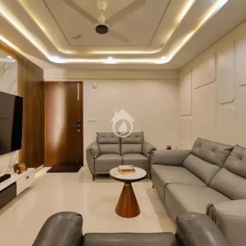 Living room with grey leather recliner sofas facing a TV wall of white marble split by brass inlays and fluted teak, a white moulded panel wall opposite